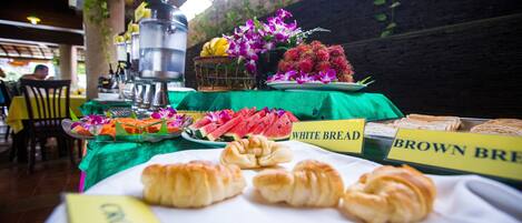 Um buffet de café da manhã com opções de pão identificadas, uma variedade de frutas e flores.