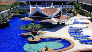 A pool area with multiple circular water features, lounge chairs, and a distinctive building with a white and red roof. - Kata Poolside Resort (Karon)