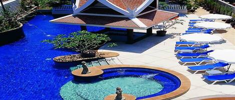 Un área de piscina con múltiples fuentes circulares, sillones reclinables y un edificio distintivo con techo blanco y rojo.