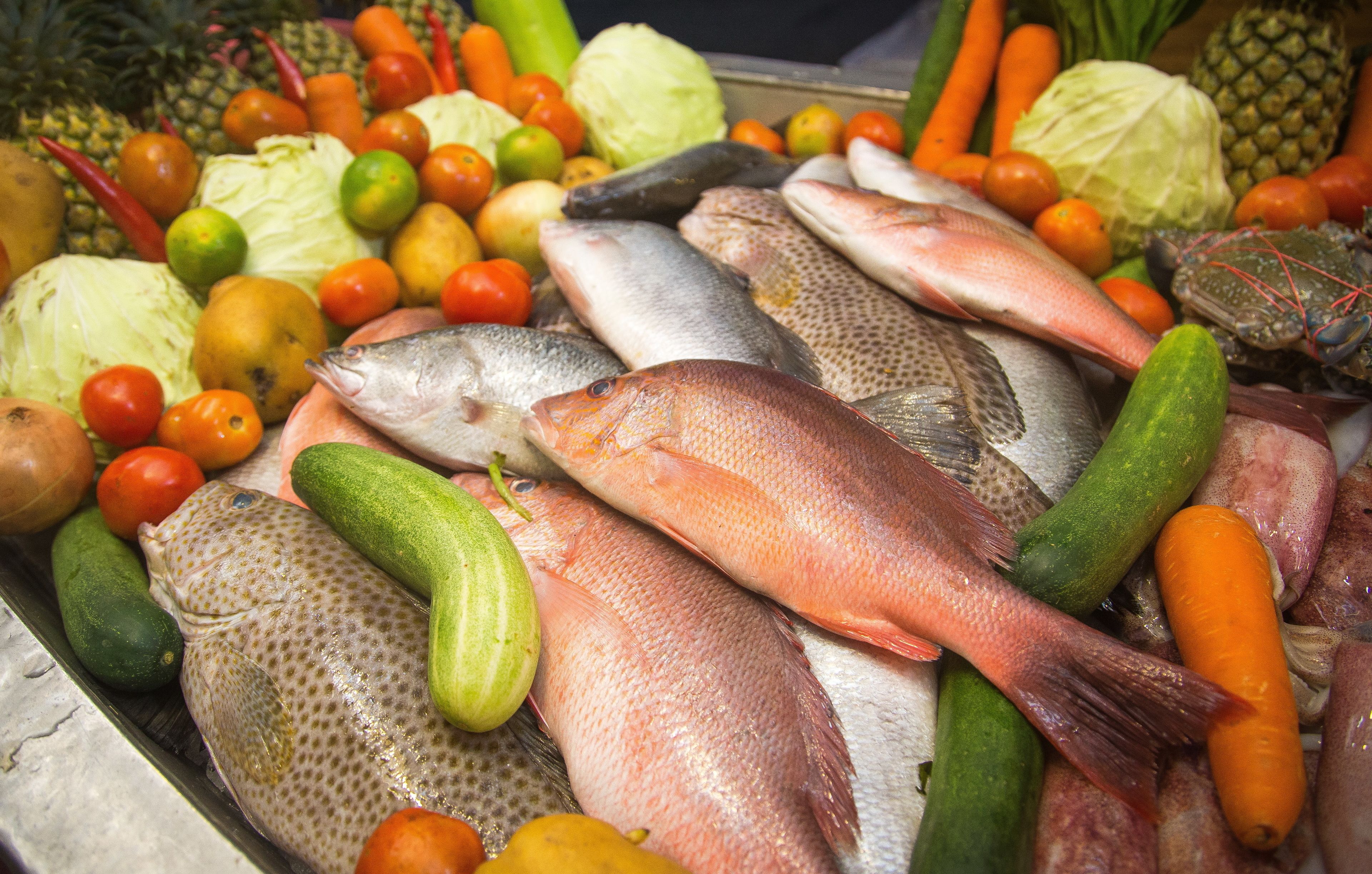 Variedad de mariscos frescos y verduras expuestos en un mercado.