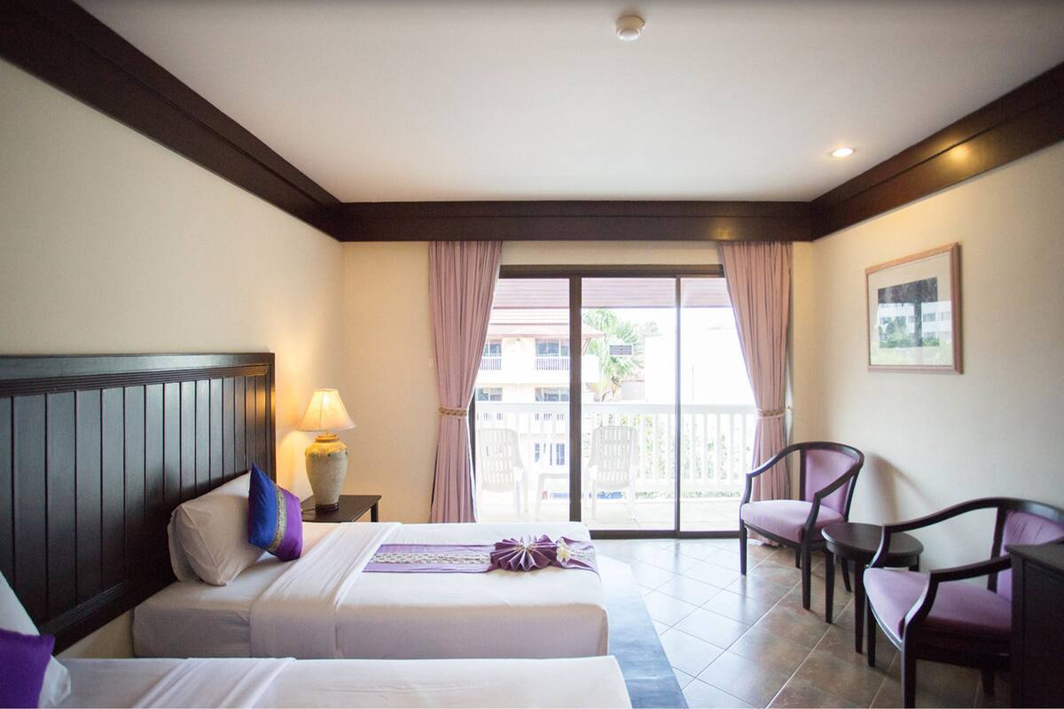 Ein Hotelzimmer mit zwei Betten, einem Balkon mit Stühlen und Blick auf Gebäude.