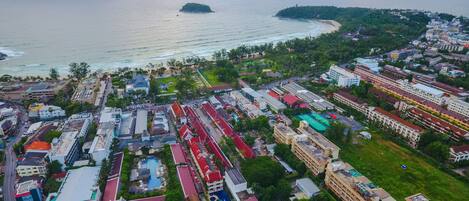 An aerial view of a coastal town with a beach, residential buildings, and a swimming pool complex.