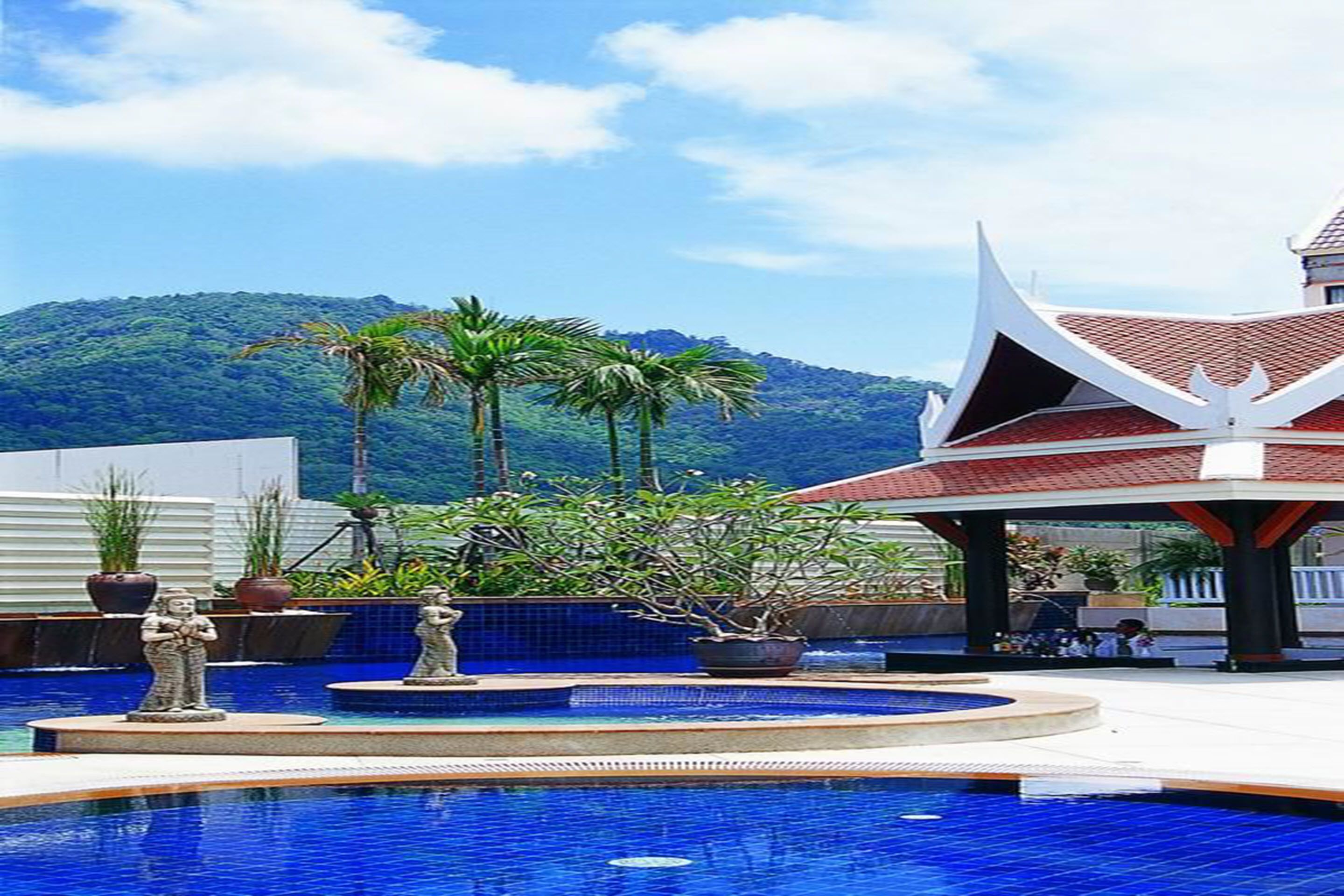 A pool area with statues, a covered pavilion, and a mountainous backdrop.