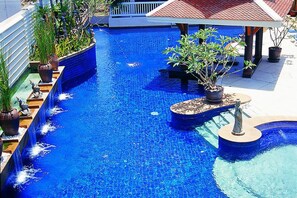 A swimming pool with a tiled edge, surrounded by potted plants and a gazebo.