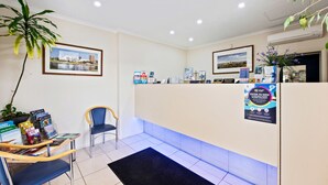A reception area with a reception desk, chairs, a black rug, framed pictures on the wall, and a potted plant. - Welcome Inn 277 (Frewville)