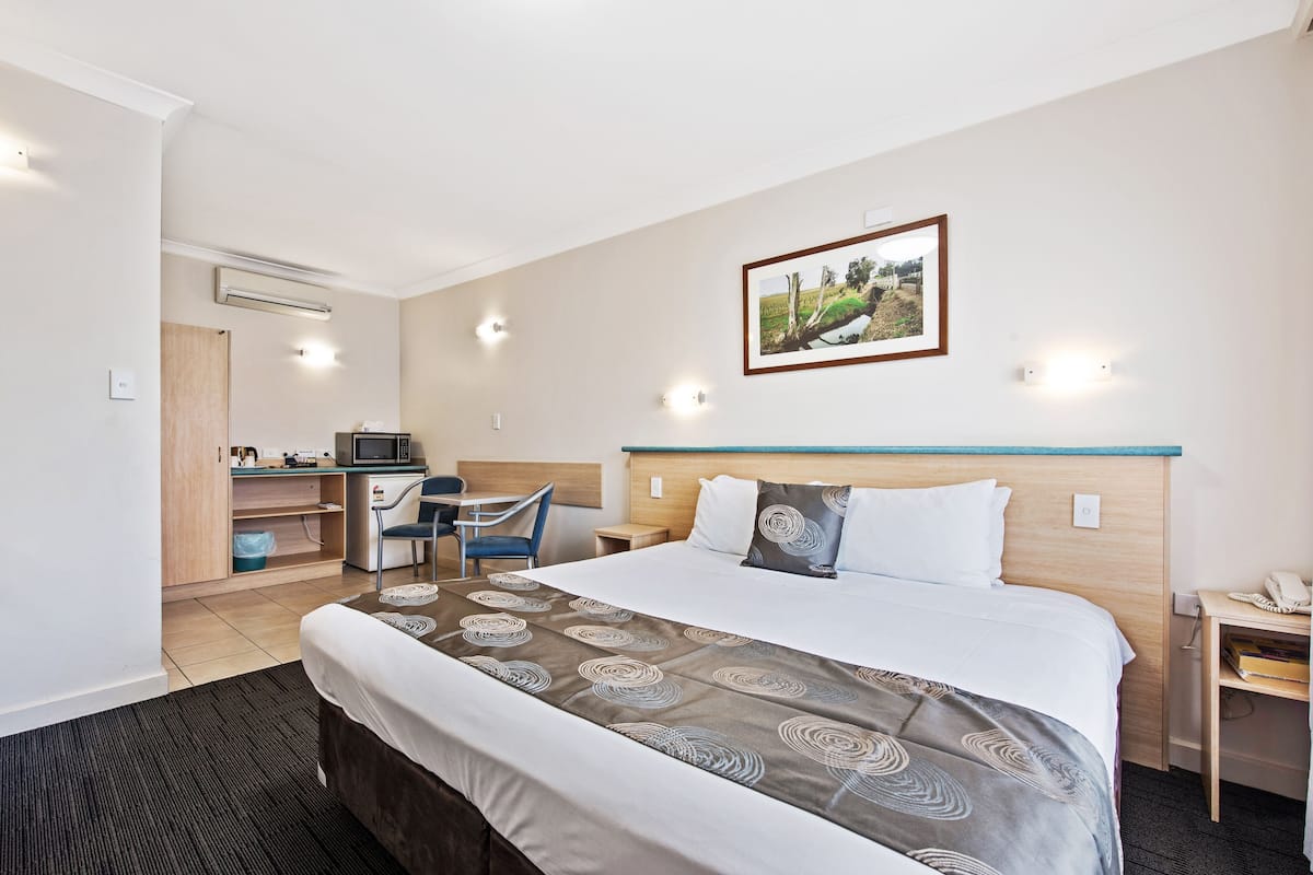 A hotel room with a bed, a desk, a chair, a microwave, and a picture on the wall.