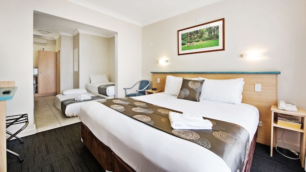 A hotel room with a large bed, a desk, a chair, and a small table with a phone. - Welcome Inn 277 (Frewville)