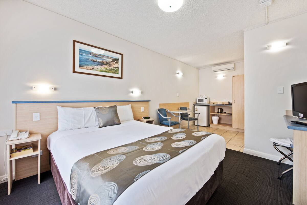 A hotel room with a bed, bedside table, lamp, desk, chair, and a television.