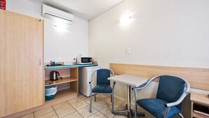 A small kitchenette with a microwave, kettle, and a sink. There are two blue chairs and a white table. - Welcome Inn 277 (Frewville)