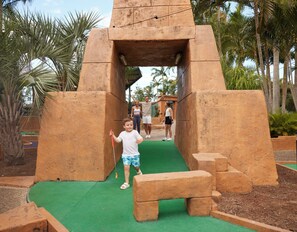 A child playing in a play structure with a green surface and palm trees in the background. - Brisbane Holiday Village (Eight Mile Plains)