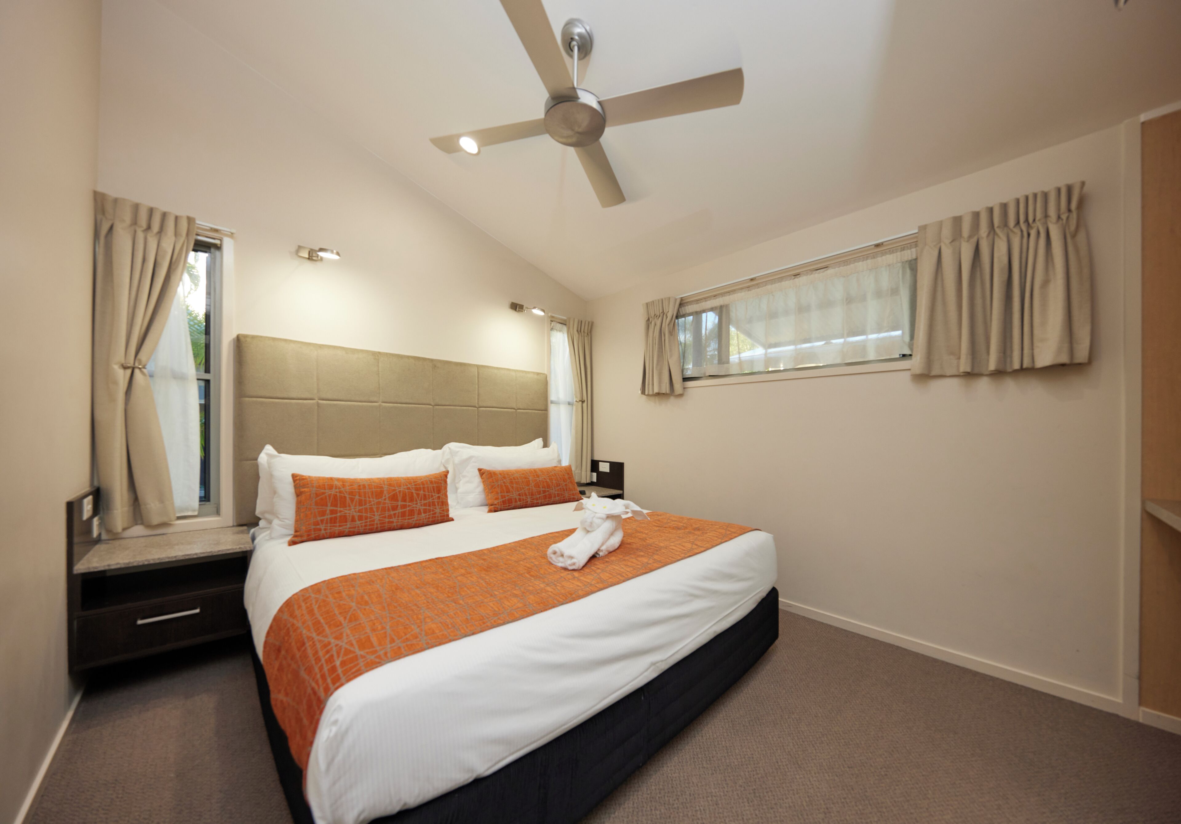 A hotel room with a large bed, a ceiling fan, a window with curtains, and a nightstand.