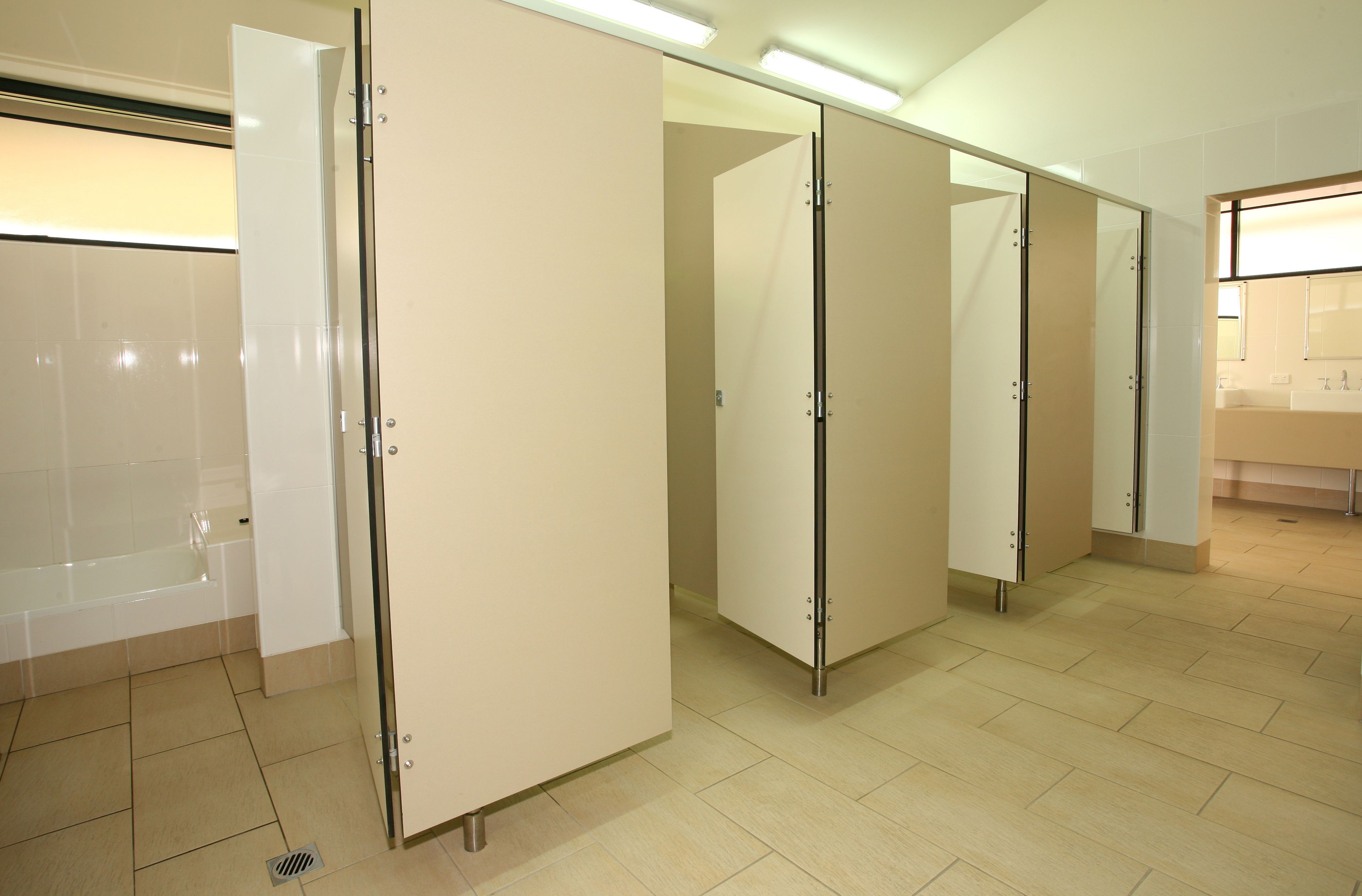 A clean, modern bathroom with a bathtub, multiple toilet stalls, and a sink area.