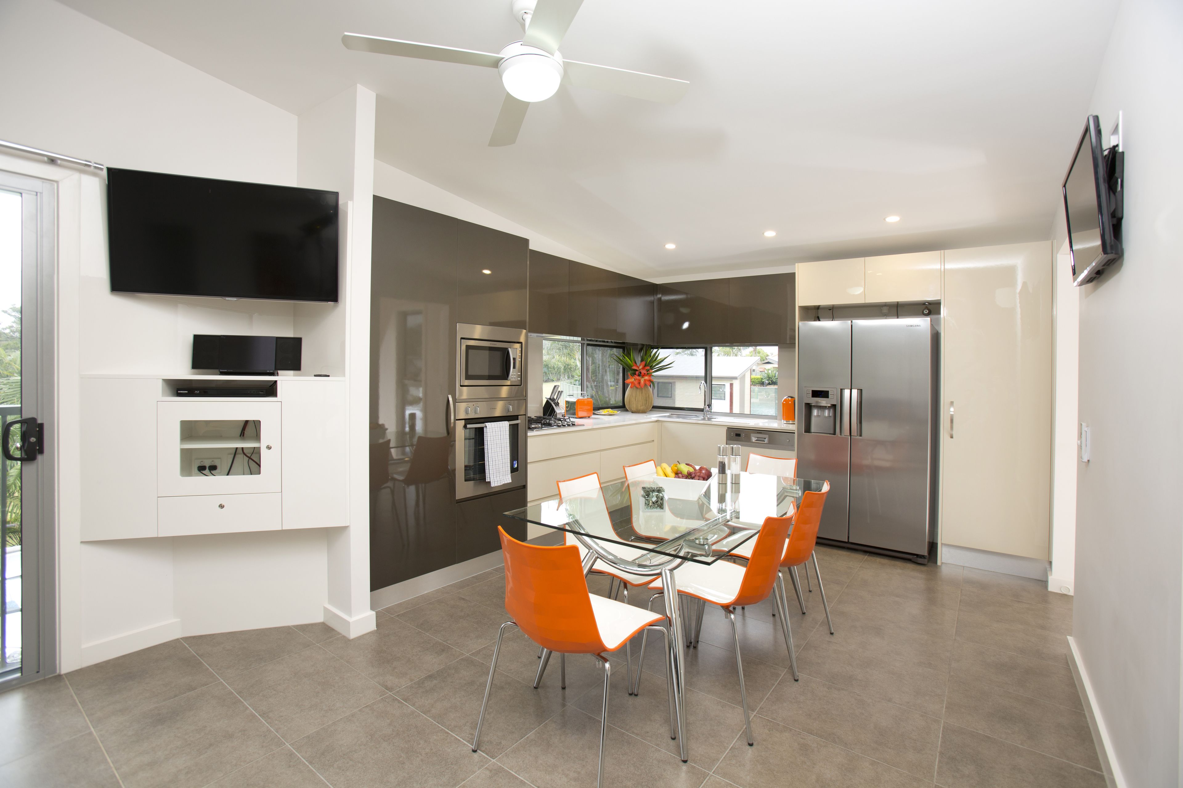 A modern kitchen with a glass dining table, stainless steel appliances, and orange chairs.