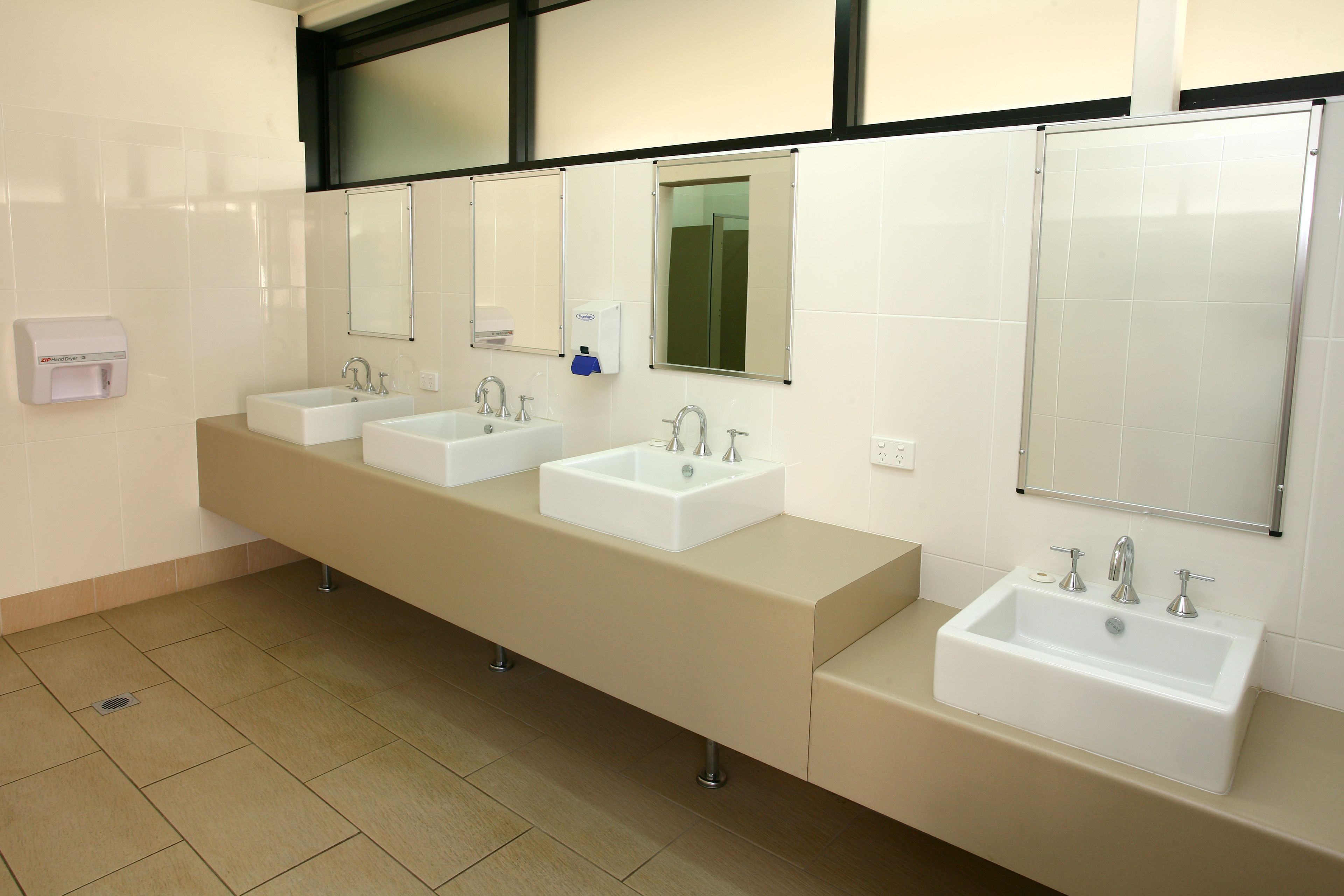 A modern bathroom with three sinks, a hand dryer, and a mirror.