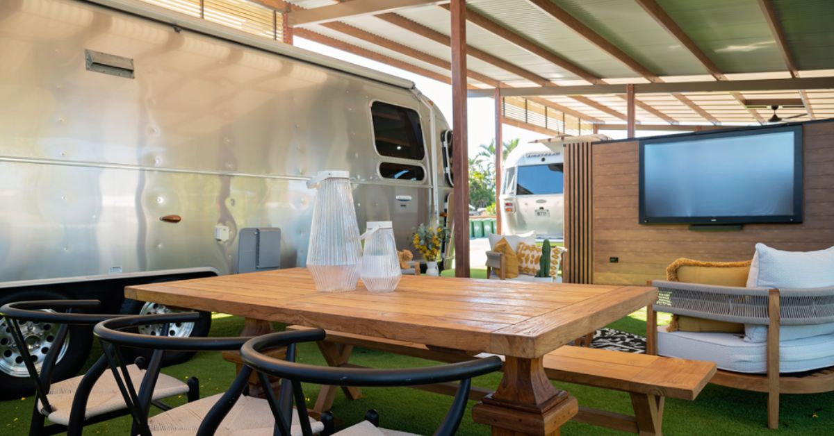 An RV with a wooden table and chairs, a TV mounted on the wall, and a covered outdoor area.