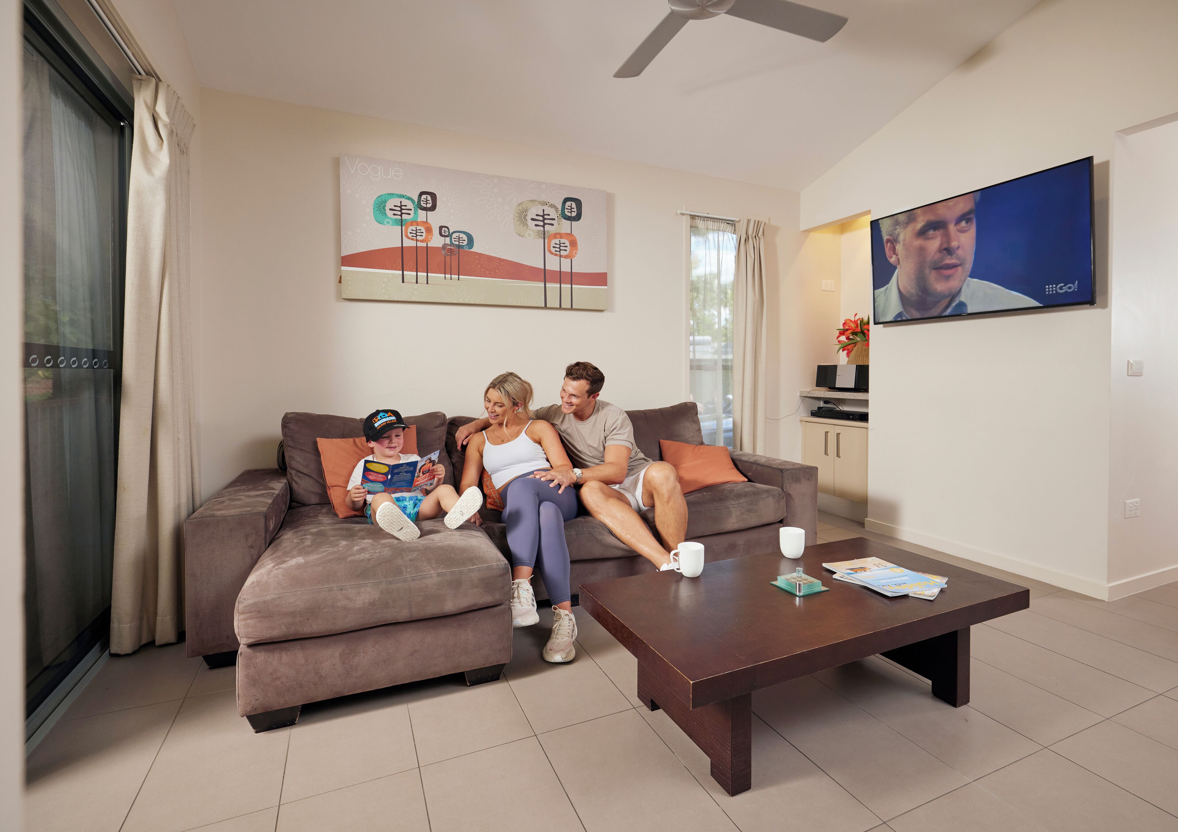 A living room with a sofa, coffee table, and a flat-screen TV mounted on the wall.