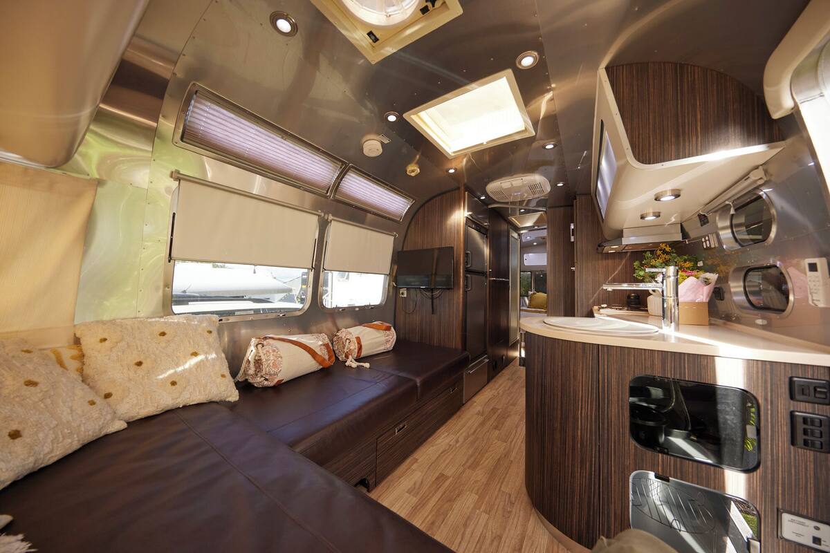 A modern RV interior with a sofa, a kitchen area, and a dining space.