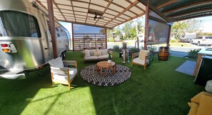 A covered outdoor area with a sofa, chairs, and a round table, adjacent to a trailer. - Brisbane Holiday Village (Eight Mile Plains)