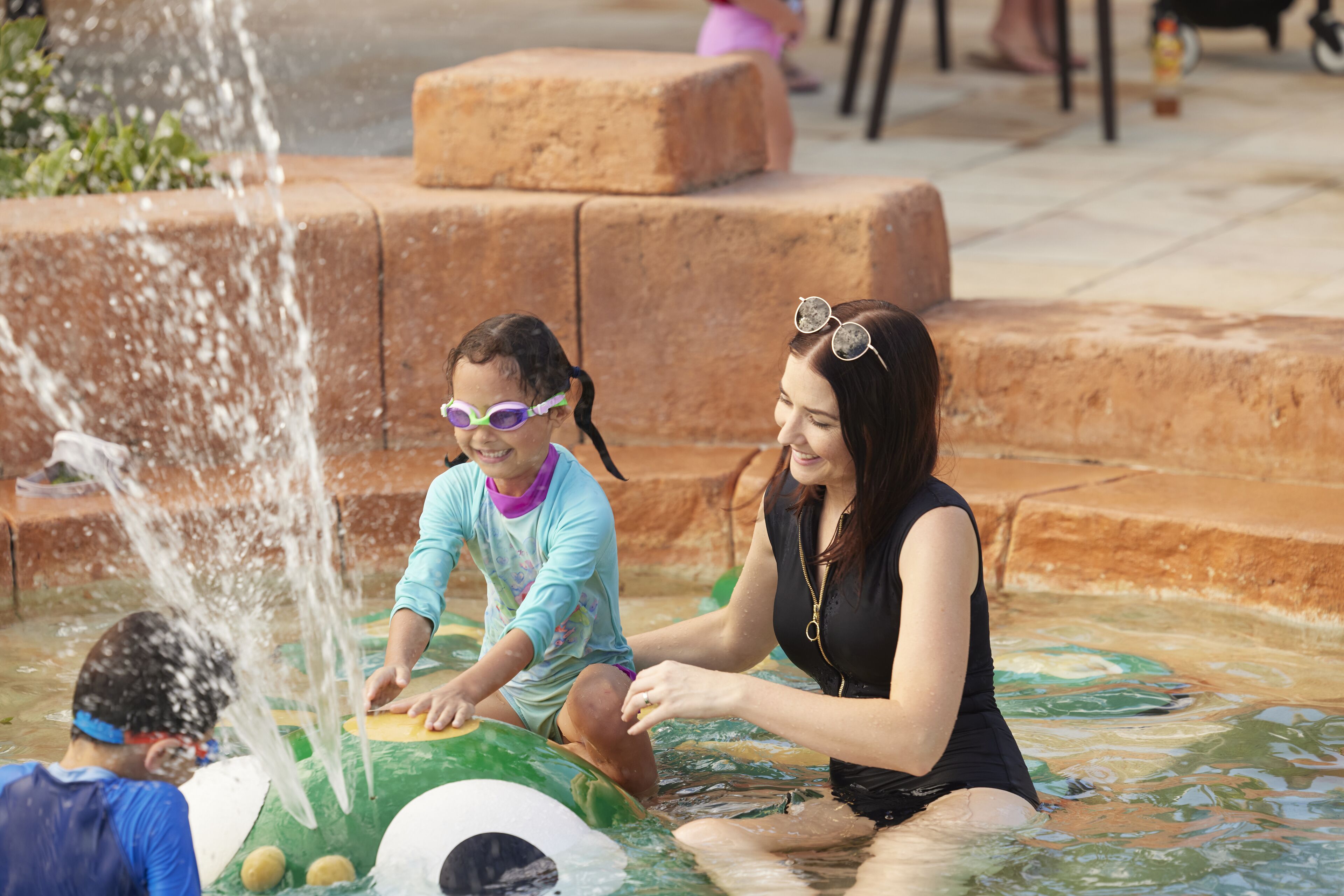 Un área de juegos con agua, niños y adultos.