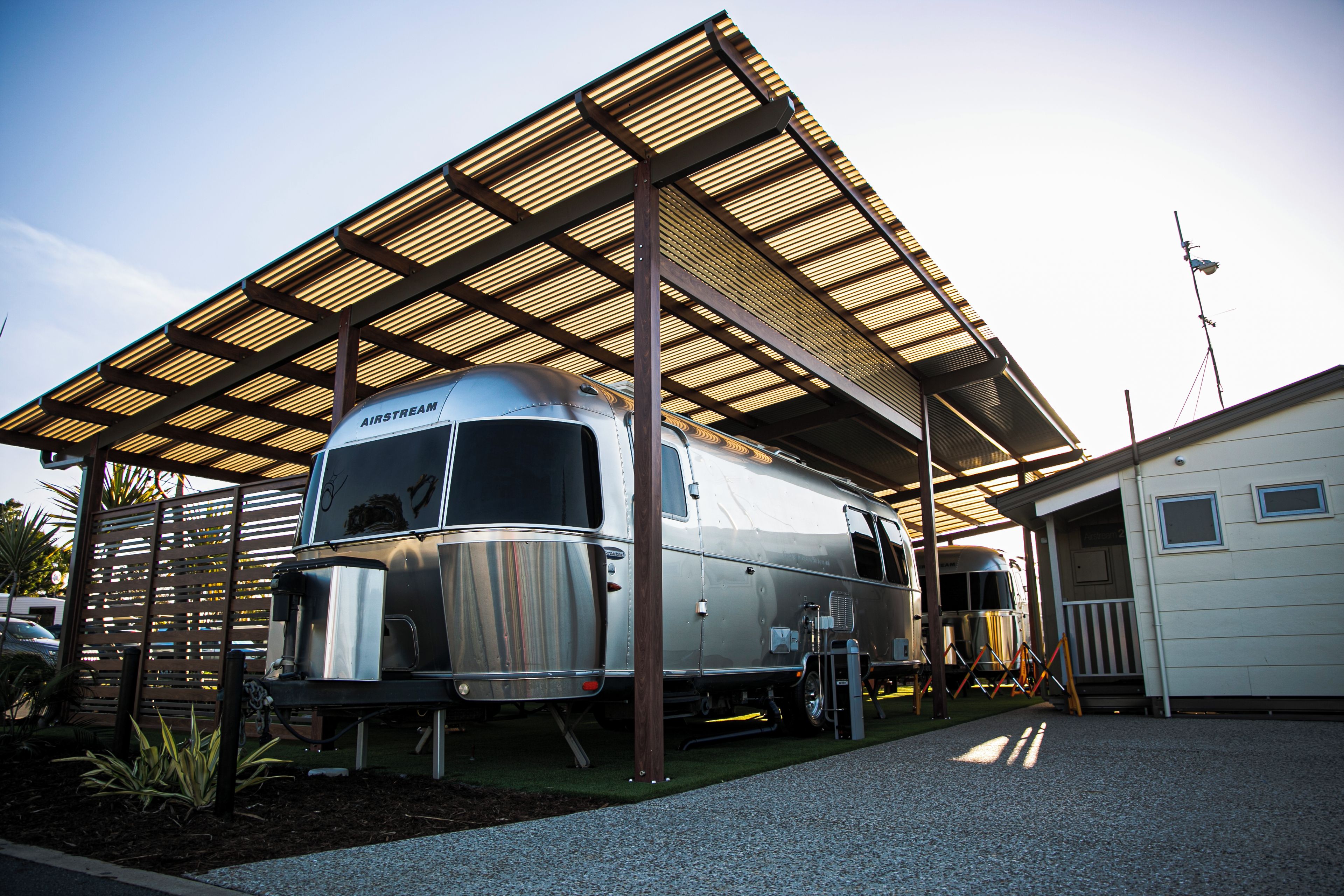 Un remolque estacionario con un área cubierta, posiblemente una casa móvil o autocaravana, aparcado bajo una estructura de techo metálico.