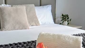 Una cama bien hecha con sábanas blancas, una flor rosa solitaria y una alfombra oscura con textura.