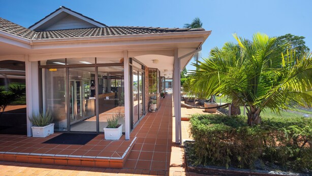 A modern building with a covered entrance, glass doors, and a tiled roof. - Island Palms Motor Inn (Forster)