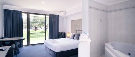 A hotel room with a bed, a desk, a chair, a bathroom with a bathtub, and a sliding glass door to the outside.