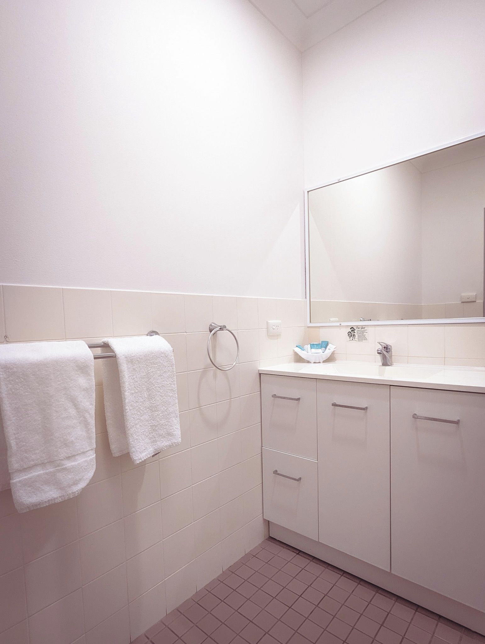 Un bagno rivestito di piastrelle bianche, un lavandino con uno specchio e due asciugamani su un porta-asciugamani.