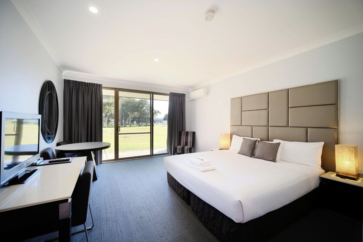 A hotel room with a bed, desk, chair, and a view of the outdoors.