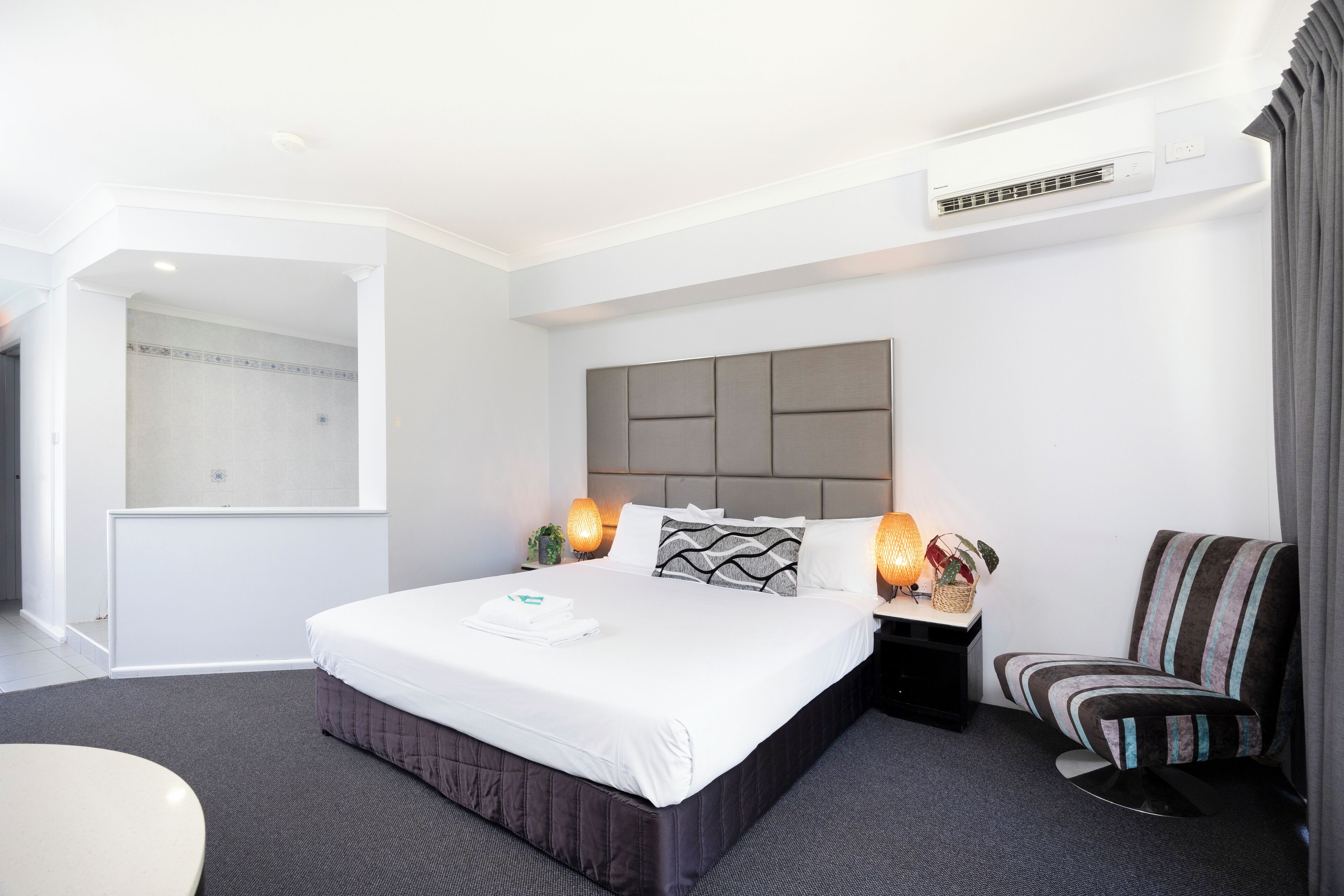 A modern hotel room with a large bed, bedside lamps, a chair, and a shower area.