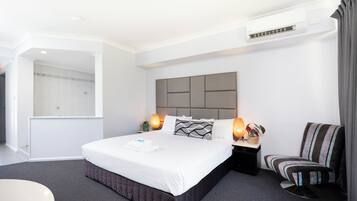 A modern hotel room with a large bed, bedside lamps, a chair, and a shower area.
