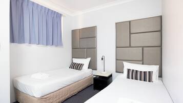 A hotel room with two beds, a nightstand, a lamp, and a window with curtains.