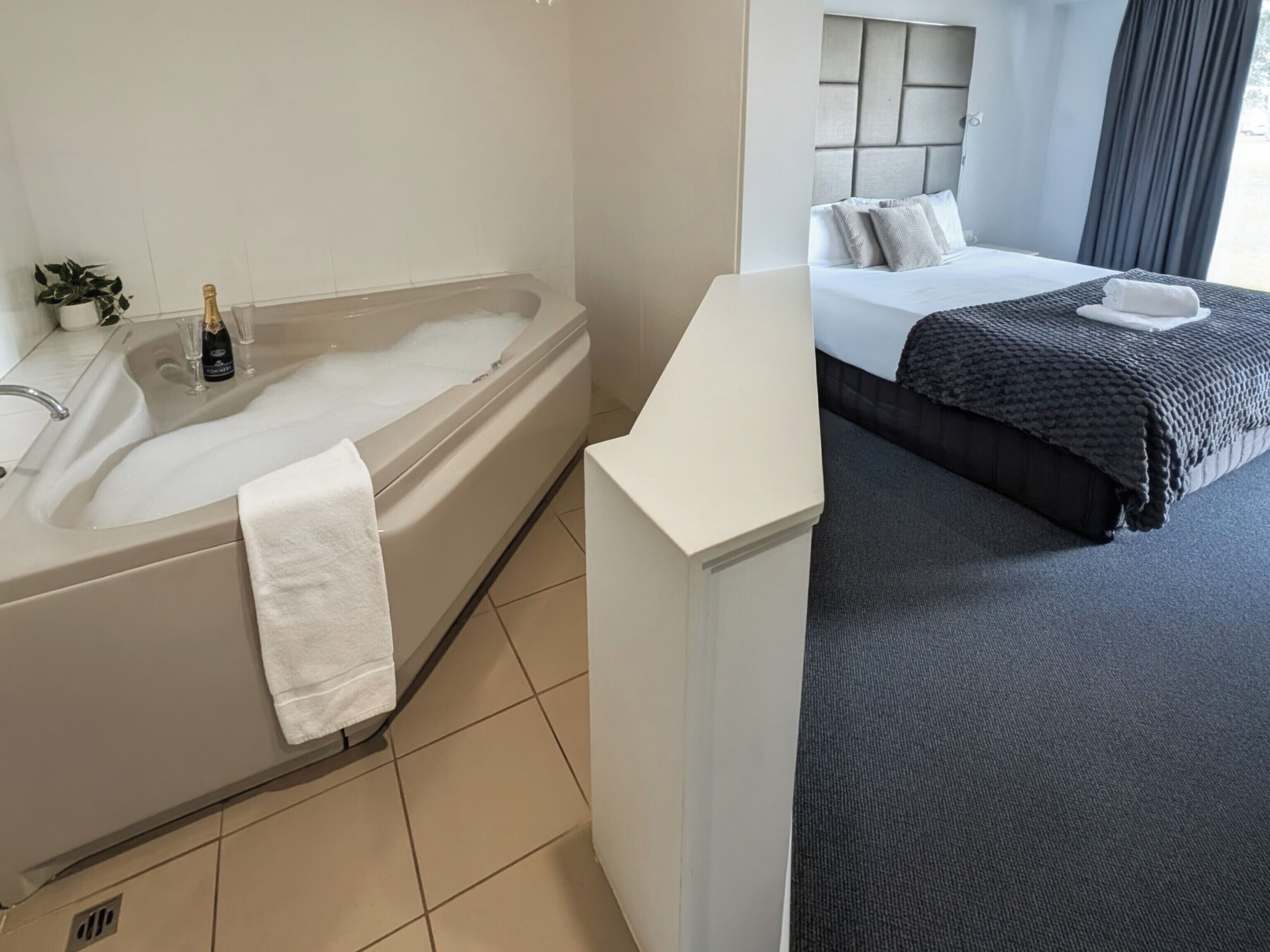 A hotel room with a bathtub, a bed, and a bedside table.