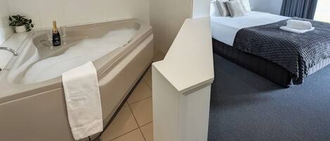 Una habitación de hotel con bañera, cama y mesita de noche.