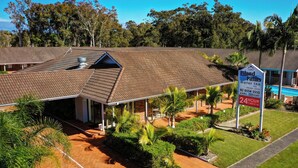 A motor inn with a tiled roof, a covered outdoor area, and a sign indicating a 24-hour check-in service. - Island Palms Motor Inn (Forster)