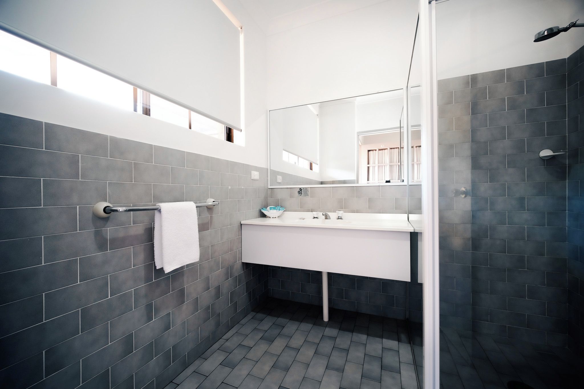 A modern bathroom with grey tiles, a white sink, and a large mirror.