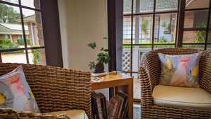 A cozy room with wicker furniture, a small wooden table with books, and a view of the outside through large windows. - Island Palms Motor Inn (Forster)