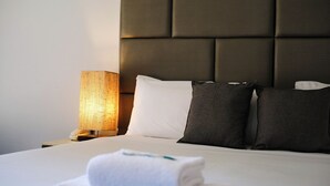 A neatly made bed with a headboard, a bedside lamp, and a folded towel on the bed. - Island Palms Motor Inn (Forster)