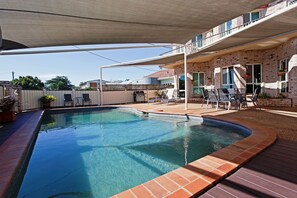 A swimming pool with a brick edge, surrounded by a deck and outdoor furniture.
