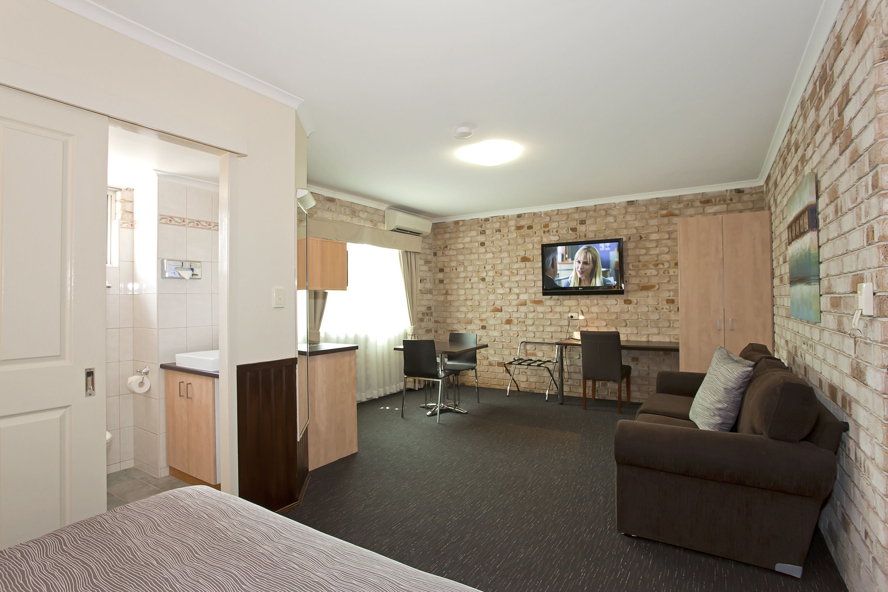 Een hotelkamer met een bed, een bureau, een bank en een televisie bevestigd aan de bakstenen muur.