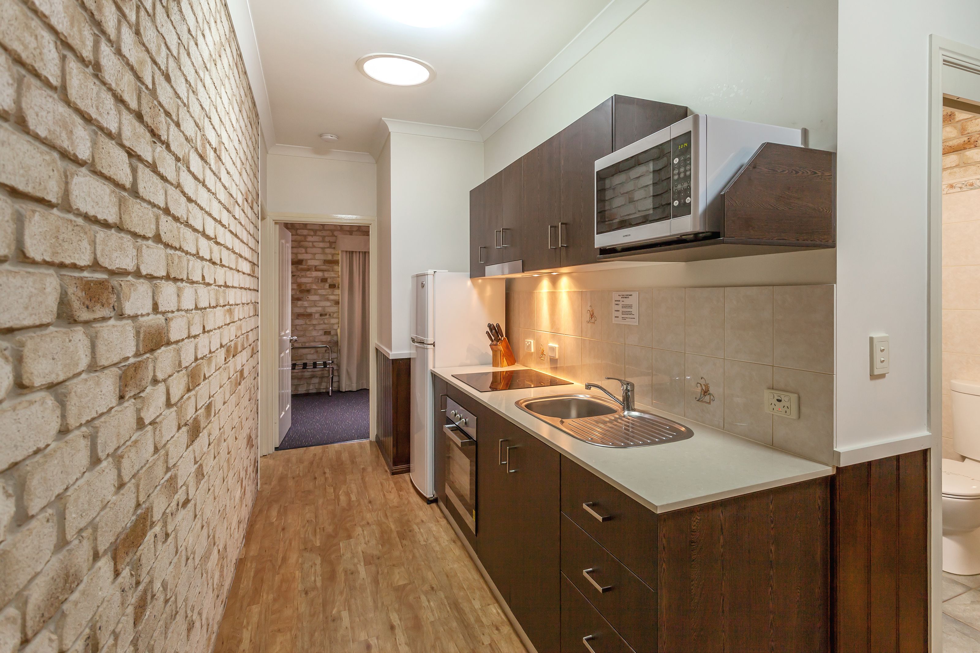 A compact kitchen with a microwave, sink, and wooden cabinets.