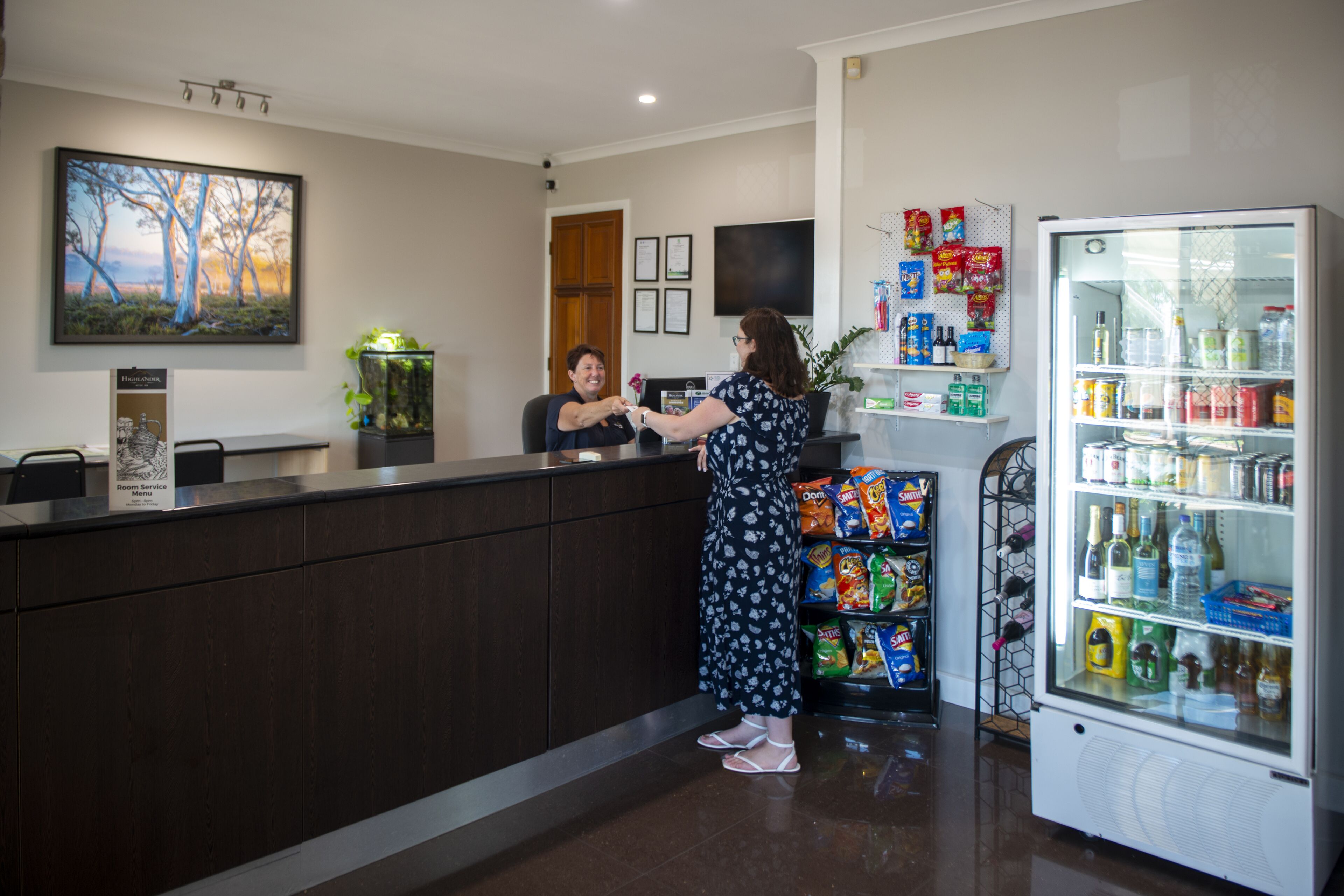 A reception area with a counter, a refrigerator stocked with beverages, and a wall-mounted television.