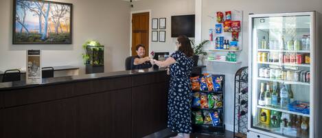 A reception area with a counter, a refrigerator stocked with beverages, and a wall-mounted television.