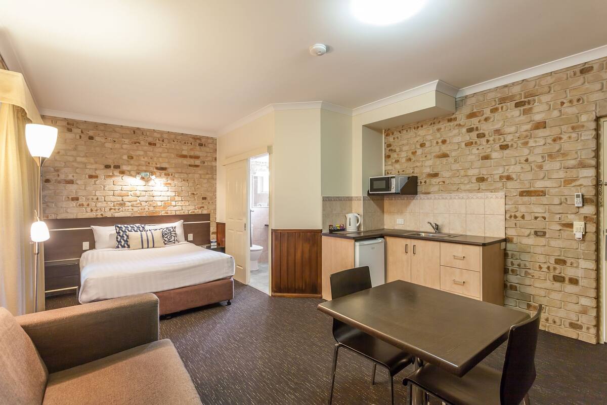 A hotel room with a bed, a desk, a chair, a kitchenette, and a bathroom.