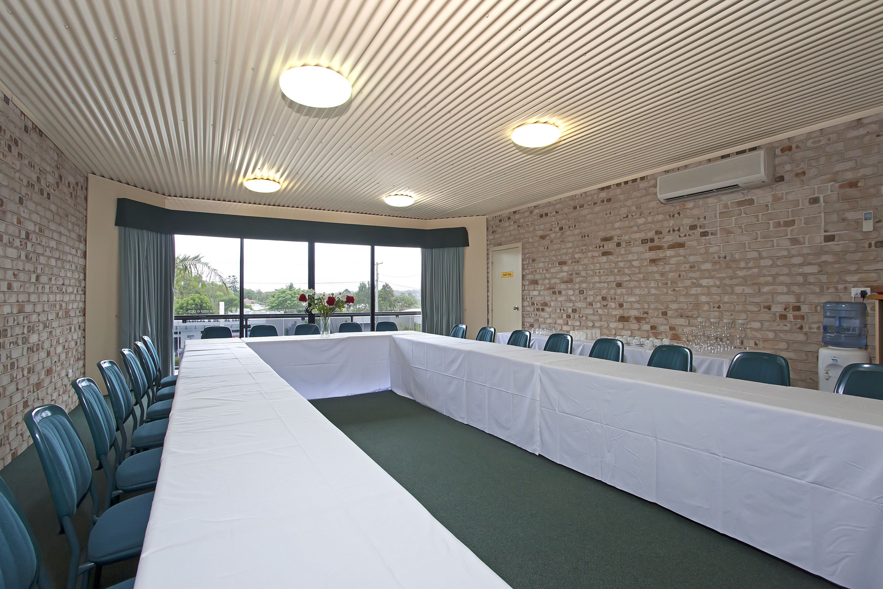 A conference room with a long table, chairs, a brick wall, and a large window.