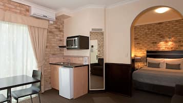 A compact hotel room with a kitchenette, a bed, a dining table, and a small seating area.