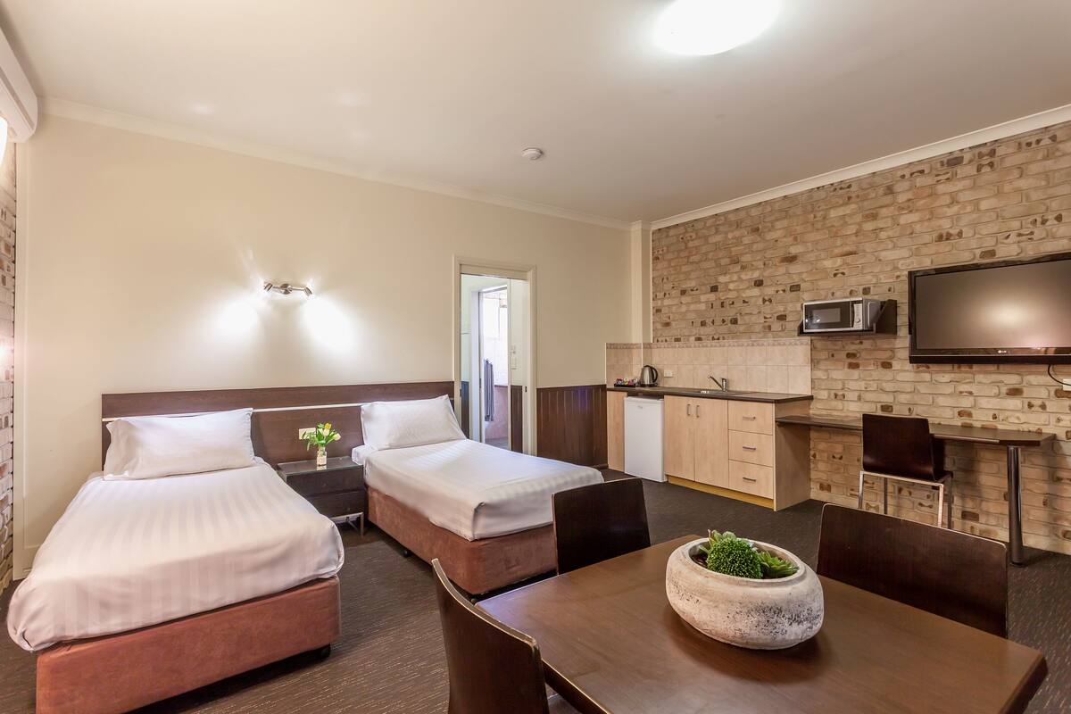A hotel room with two beds, a dining table with chairs, a microwave, and a television on the wall.