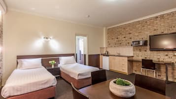 A hotel room with two beds, a dining table with chairs, a microwave, and a television on the wall.