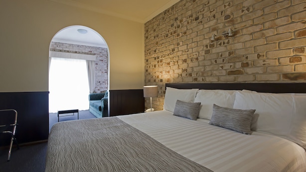 A hotel room with a large bed, a brick wall, and a desk with a chair.