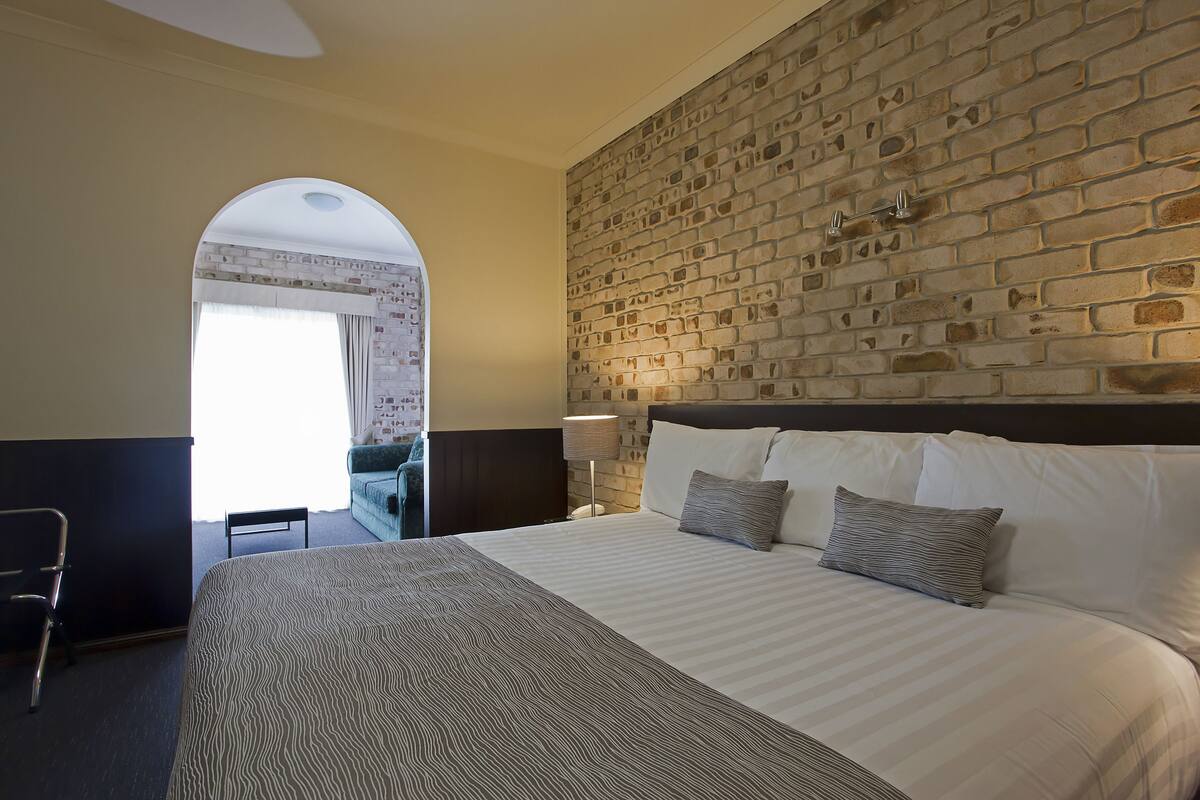 A hotel room with a large bed, a brick wall, and a desk with a chair.